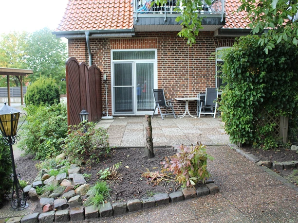 FeWo "An der Hache" Ziegelhaus mit heller Terrasse, umgeben von Pflanzen und Gartenmöbeln, bei sonnigem Wetter.