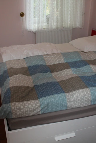 Wohnzimmer mit Holzboden und einem Doppelbett, dekoriert mit einem karierten Bettbezug in blau-braunen Tönen.