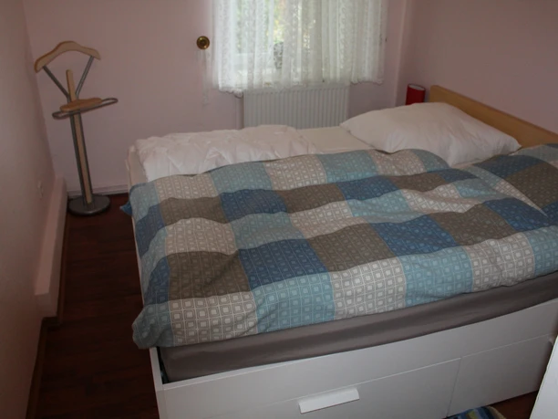Woonkamer met houten vloer en een tweepersoonsbed, gedecoreerd met een geruit dekbedovertrek in blauwbruine tinten.