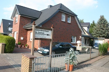Bakstenen huis van twee verdiepingen met parkeerplaats en een bord "Gastenflat in het centrum" in de voortuin.
