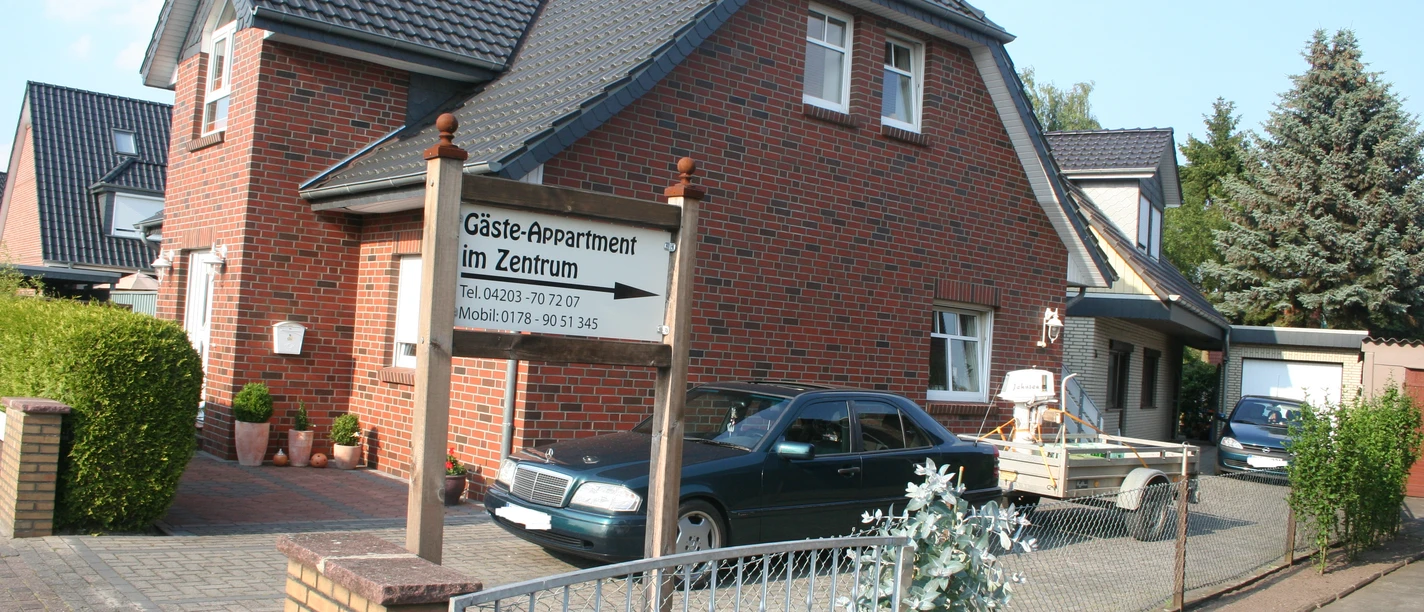 Two-storey brick house with parking space and a sign "Gäste Appartement im Zentrum" in the front garden.