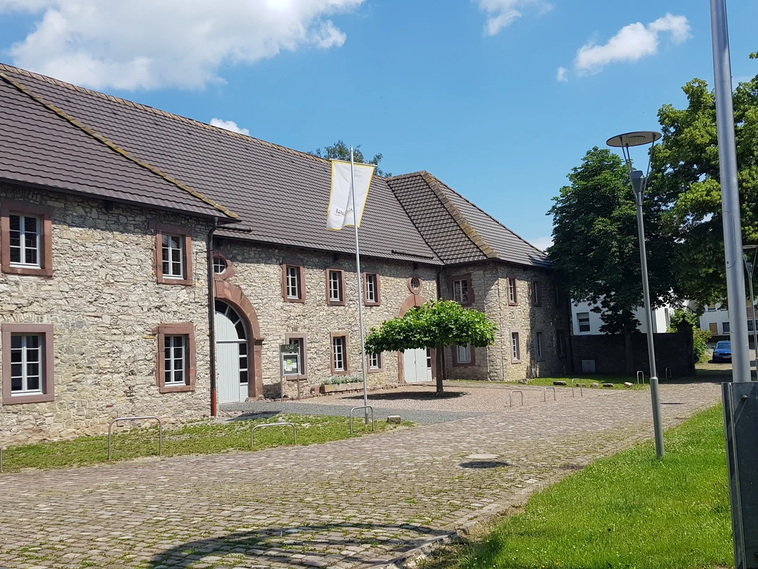 wiemers_meyerscher_hof_ottbergen (1).jpg Eine historische Hofanlage aus Stein mit Satteldächern, umgeben von gepflasterten Wegen und grünen Bäumen.