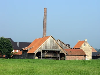 Ziegelei Rheda-Wiedenbrück Altes Ziegelwerk mit hohem Schornstein und roten Dächern auf einer Wiese unter blauem Himmel.