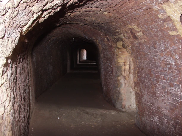 Ziegelei Ringofen Dunkler, gemauerter Tunnel mit gewölbter Decke und einem leichten Lichtschein am Ende.
