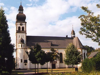 Barockkirche mit Zwiebeltürmen und Garten im Vordergrund, sonniger Himmel im Hintergrund.