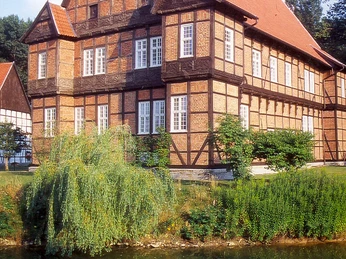 Haus Aussel Fachwerkhaus mit rotem Satteldach, umgeben von Grün und einem Teich. Reflektion im Wasser.