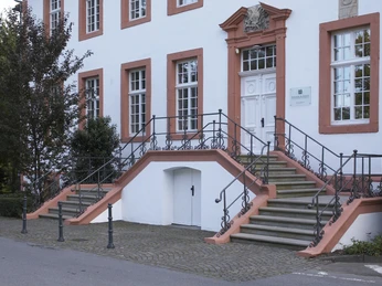 Historisches Gebäude mit symmetrischer Treppe, weißen Fensterrahmen und korallenfarbenen Details.
