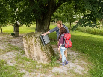 Eisernes Buch Andepen Zwei Menschen betrachten ein offenes, metallisches Buch auf einem Moos-bedeckten Stein unter einem Baum.