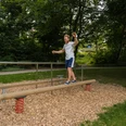 Balance Bewegungsparcours Bad Wünnenberg Ein Mann balanciert in einem grünen Park auf einem Holzstamm mit Sprungfedern an den Enden.