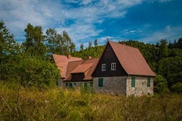 Aahäuser bei Bleiwäsche Altes Fachwerkhaus mit roten Ziegeldächern, umgeben von dichter, grüner Vegetation unter blauem Himmel.