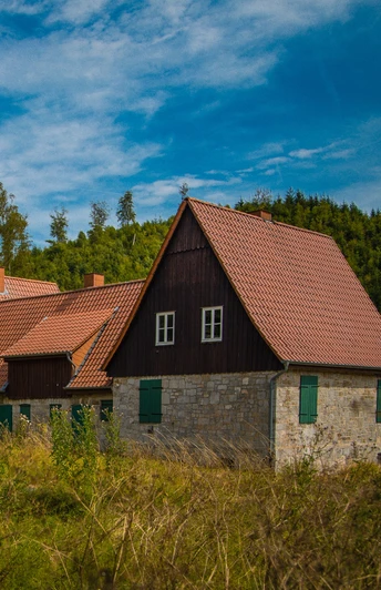 Aahäuser bei Bleiwäsche Altes Fachwerkhaus mit roten Ziegeldächern, umgeben von dichter, grüner Vegetation unter blauem Himmel.