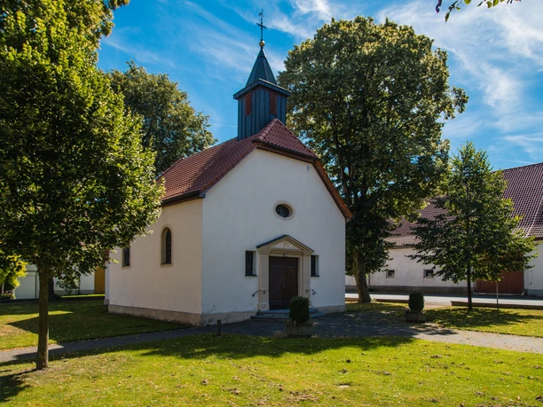 Kapelle in Elisenhof Weiße Kapelle mit rotem Satteldach und kleinem Turm, umgeben von grünen Bäumen im Sommer.