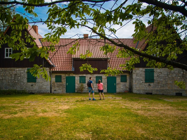 Wanderer bei den Aahäusern Zwei Wanderer stehen vor den historischen Aahäusern, umgeben von grüner Natur und altem Gemäuer.