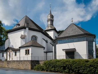 St. Antonius Kirche in Bad Wünnenberg mit weiße Fassade, markantem Turm und umgeben von grüner Hecke.