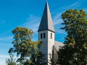 Kirche Helmern Kirche Helmern mit schlankem Turm vor blauem Himmel, umgeben von Bäumen, Schafe grasen auf Wiese.