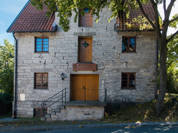 Ohrmackers Mühle in Haaren Historische steinerne Mühle mit roten Dachziegeln, umgeben von grünen Bäumen an einem sonnigen Tag.