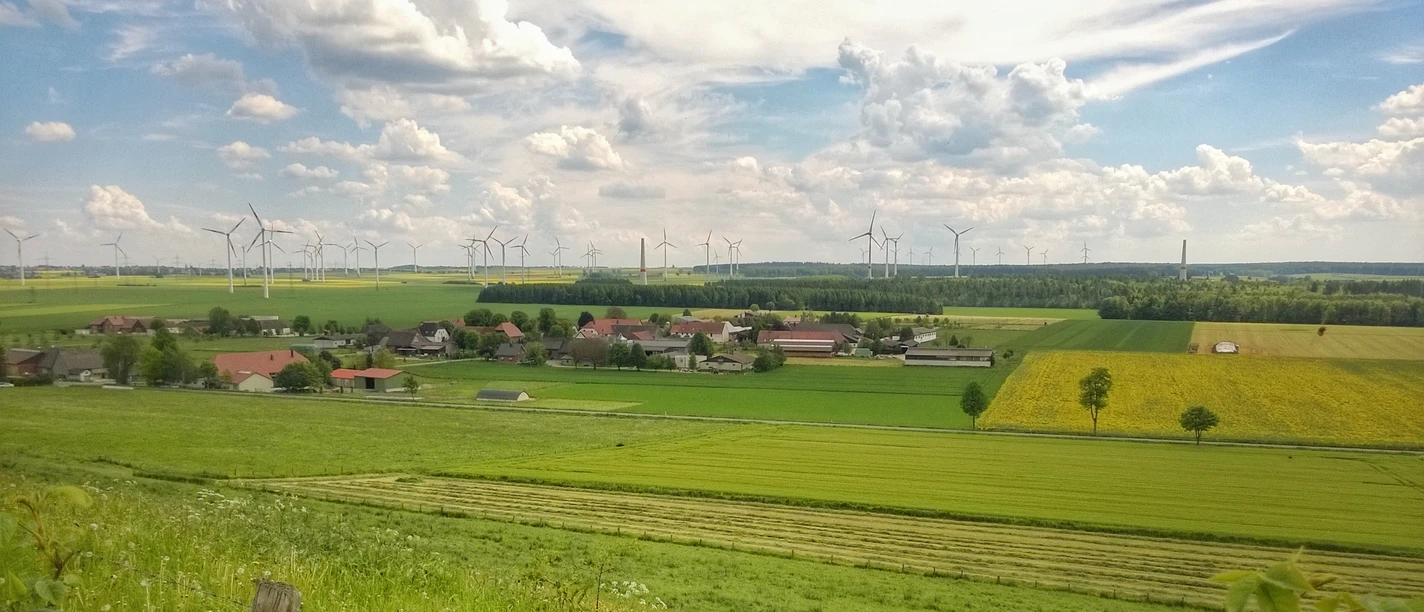 Ortsansicht Elisenhof Ländliche Szene des Elisenhofs mit Windrädern im Hintergrund und weitem grünem Feld im Vordergrund.