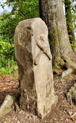 Totenkopfstein Steinerner Totenschädel-Monolith im Wald, umrahmt von Bäumen und Wurzeln an einem sonnigen Tag.