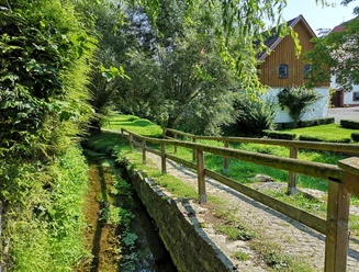 Mühlengraben in Brakel-Bellersen Kleiner Bachlauf mit Holzgeländer, angrenzenden Wiesen und Bäumen, im Hintergrund ein Fachwerkhaus.