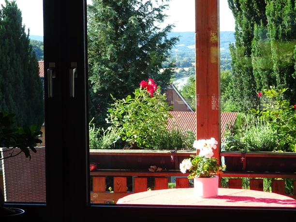 Aussicht Ferienwohnung Jakobs Blick durch ein Fenster auf farbenprächtige Blumen, Wälder und ferne Hügel einer weitläufigen Landschaft.