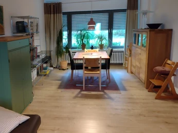 Wohnbereich Ferienwohnung Jakobs Heller Wohnbereich mit Esstisch, Stühlen, Pflanzen und Möbeln aus Holz, große Fenster im Hintergrund.