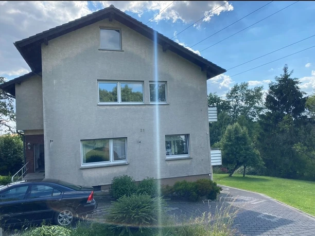 Fewo Julia Außenansicht.jpg Zweistöckiges Wohnhaus mit Garten und gepflasterter Einfahrt, blauer Himmel und Wolken im Hintergrund.