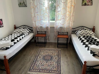 Schlafzimmer Zwei Einzelbetten mit schwarz-weiß gemusterten Bettdecken, ein Fenster mit Vorhang und zwei Nachttische.