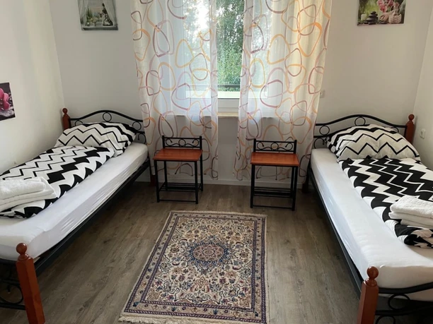 Schlafzimmer Zwei Einzelbetten mit schwarz-weiß gemusterten Bettdecken, ein Fenster mit Vorhang und zwei Nachttische.