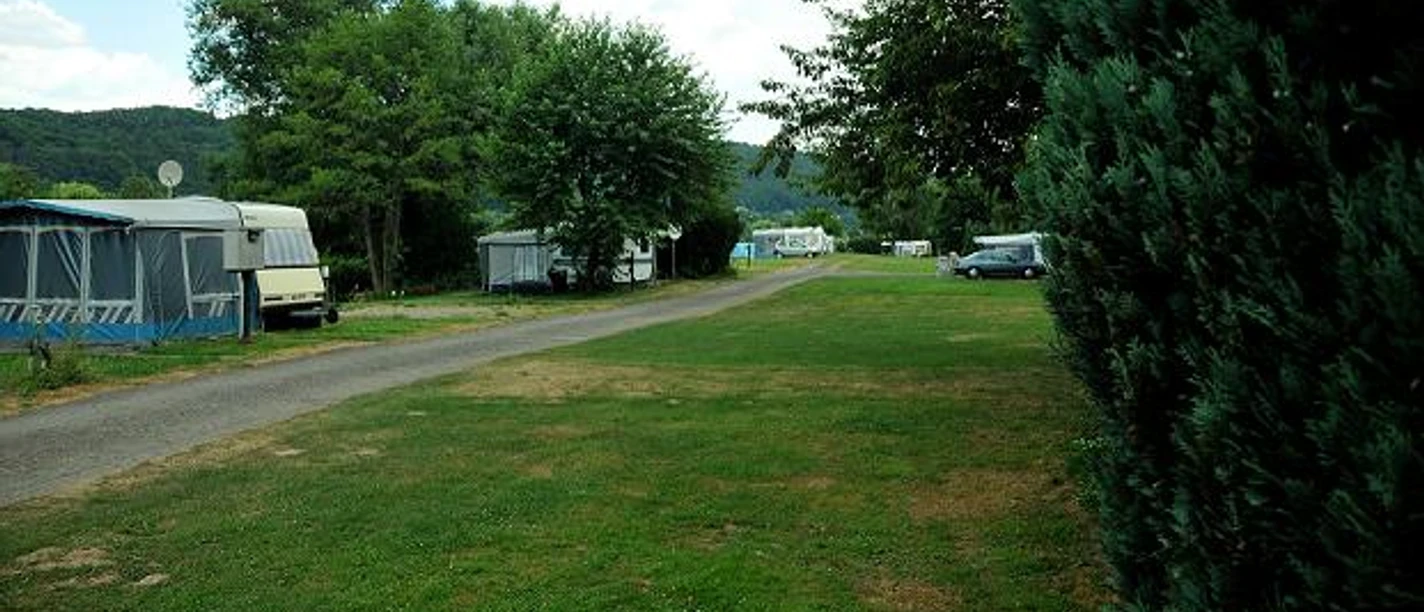 Stellplätze Naturcamp an der Weser Grüne Wiesengelände mit Wohnwagen und Wohnmobilen, von Bäumen gesäumt, nahe eines Flussufers.