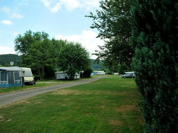 Stellplätze Naturcamp an der Weser Grüne Wiesengelände mit Wohnwagen und Wohnmobilen, von Bäumen gesäumt, nahe eines Flussufers.
