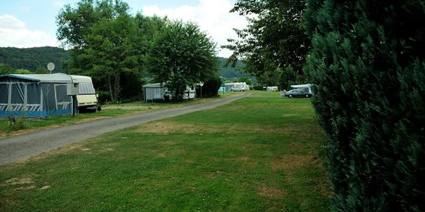 Stellplätze Naturcamp an der Weser Grüne Wiesengelände mit Wohnwagen und Wohnmobilen, von Bäumen gesäumt, nahe eines Flussufers.