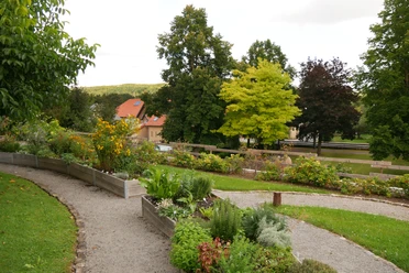 Sinnesgarten in Germete Verschlungene Kieswege führen durch den blühenden Sinnesgarten, umgeben von Bäumen und Hochbeeten.