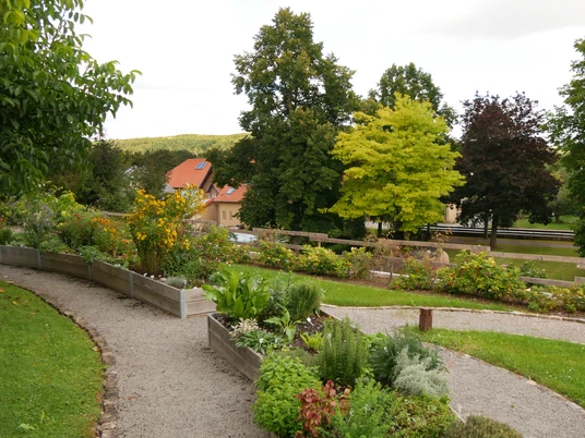 Sinnesgarten in Germete Verschlungene Kieswege führen durch den blühenden Sinnesgarten, umgeben von Bäumen und Hochbeeten.