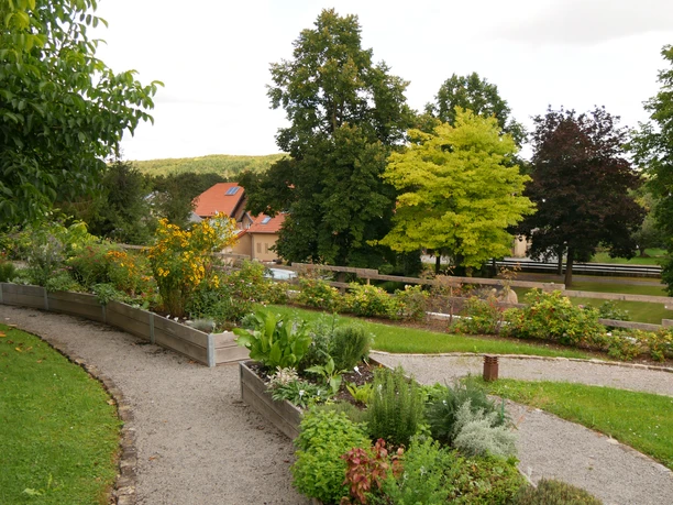 Sinnesgarten in Germete Verschlungene Kieswege führen durch den blühenden Sinnesgarten, umgeben von Bäumen und Hochbeeten.