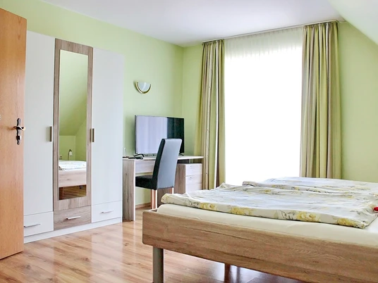 Zimmer Helles Schlafzimmer mit zwei nebeneinander stehenden Einzelbetten, Schreibtisch und TV, Holzboden.