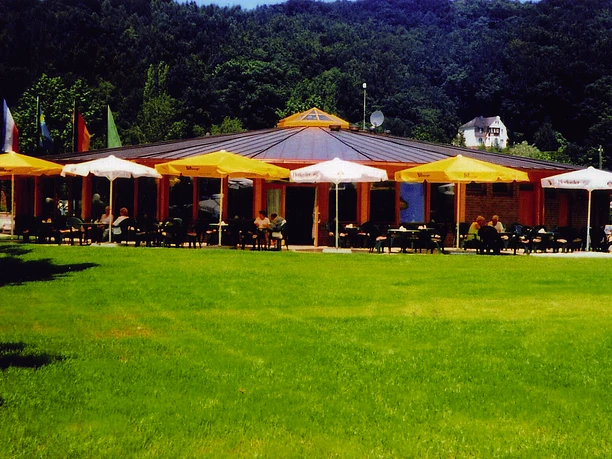 Restaurant auf einem Campingplatz mit runden Dach und Außenterrasse, umgeben von grüner Wiese.
