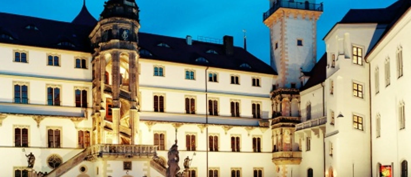 Illuminated Hartenfels Castle in the evening light with striking tower and courtyard view.