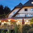 Deekes Quellenhof Ein Landhaus bei Abenddämmerung mit beleuchteter Terrasse und bunten Sonnenschirmen im Vordergrund.