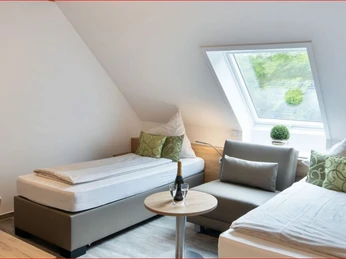 Deekes Quellenhof Zwei Betten in einem modernen, hellen Zimmer mit Dachfenster und gemütlicher Sitzecke.