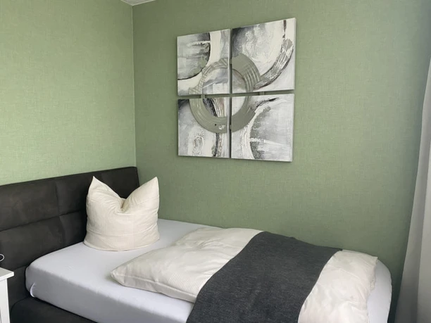 Hotel-und-Restaurant-Borchard-1.jpg Ein Einzelzimmer mit grauem Bett, weißem Kissen und moderner Kunst an einer grünen Wand.