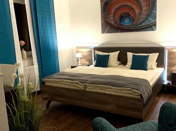 Hotel-und-Restaurant-Borchard-3.jpg Ein gemütliches Hotelzimmer mit Doppelbett, blauen Akzenten und einem spiralförmigen Kunstwerk an der Wand.