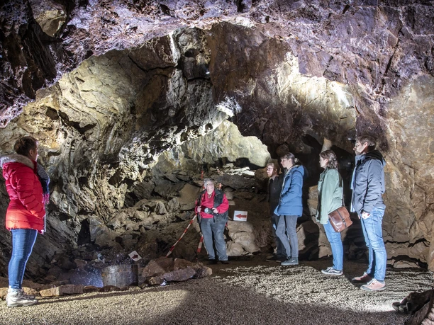 Aggertalhöhle Fünf Personen erkunden eine beleuchtete Höhle mit unebenen Wänden in einer geführten Tour.