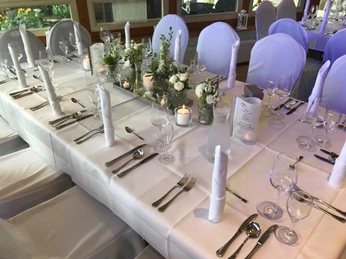 Dreimädelhaus Festlich gedeckter Tisch mit weißen Tischdecken, eleganten Blumengestecken und Kerzenarrangements.