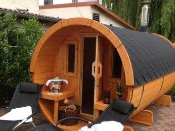 Dreimädelhaus Eine runde Holzsauna in Fassform steht im Freien, umgeben von grüner Vegetation.