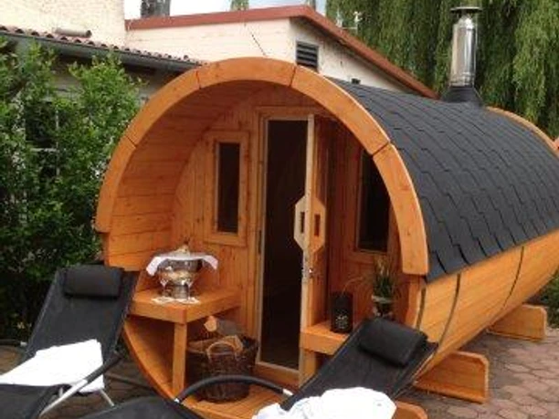 Dreimädelhaus Eine runde Holzsauna in Fassform steht im Freien, umgeben von grüner Vegetation.