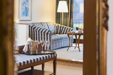Berggasthof Wilhelmshöhe Eleganter Hotelwohnbereich mit blau-weiß gestreiftem Sofa, Tisch voller Gläser und Entspannungsmöbeln.