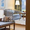 Berggasthof Wilhelmshöhe Eleganter Hotelwohnbereich mit blau-weiß gestreiftem Sofa, Tisch voller Gläser und Entspannungsmöbeln.