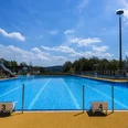 Panoramabad Engelskirchen Freibad mit blauem Schwimmbecken, Sprungbrettern und Rutsche an einem sonnigen Tag mit Wolken am Himmel.