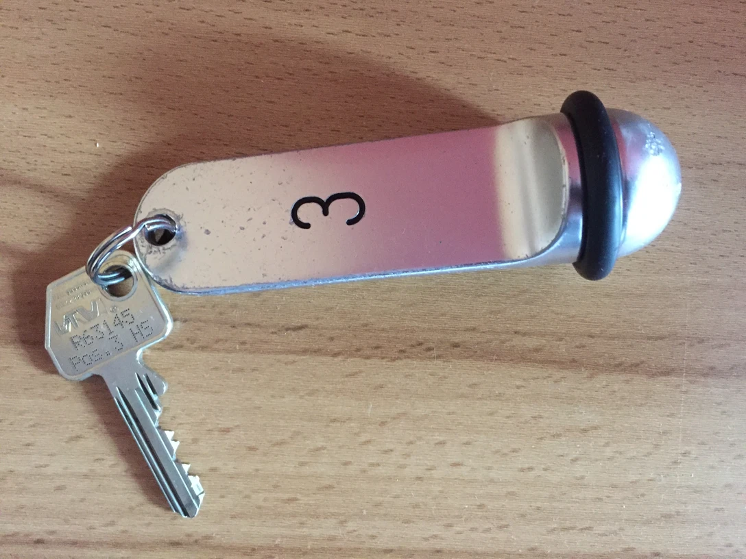 Schlüssel Ein einfacher Metallschlüssel mit Anhänger, graviert mit der Zahl 3, liegt auf einer hölzernen Oberfläche.