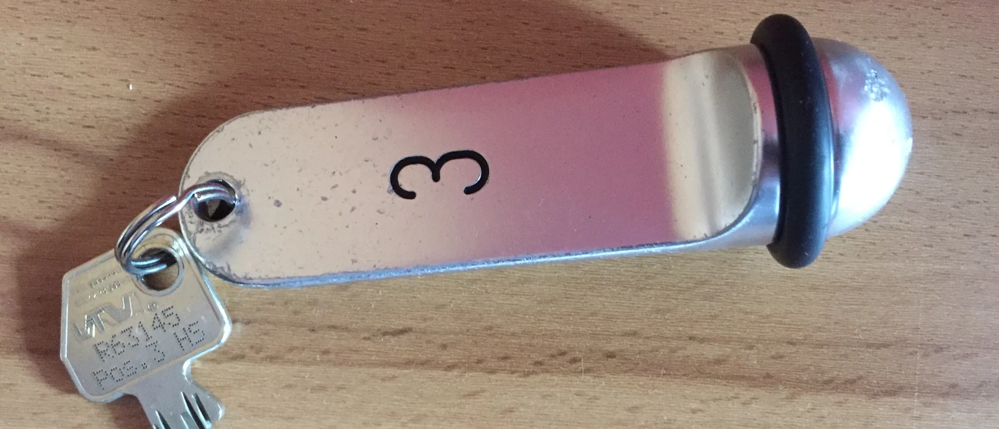 Schlüssel Ein einfacher Metallschlüssel mit Anhänger, graviert mit der Zahl 3, liegt auf einer hölzernen Oberfläche.